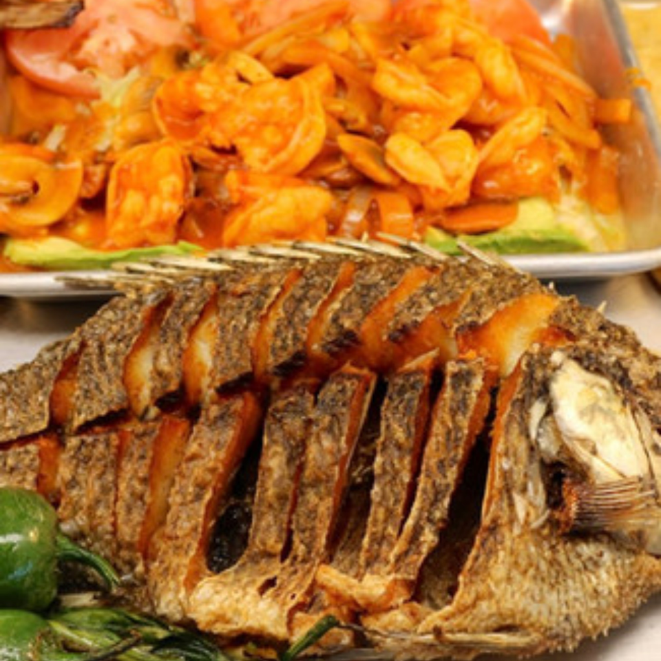 Whole fried fish with sliced green peppers and a dish of shrimp in red sauce.
