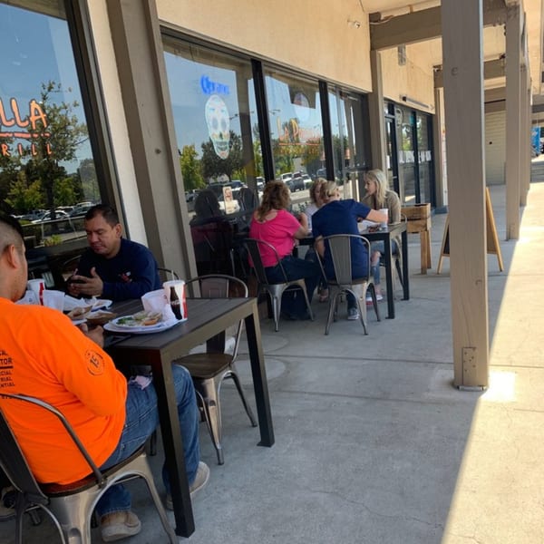 Patrons enjoying Mexican food and drinks at outdoor tables on the La Parrilla Taqueria patio.