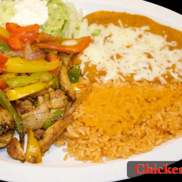 Chicken fajitas with bell peppers, onions, rice, refried beans, guacamole, and sour cream.