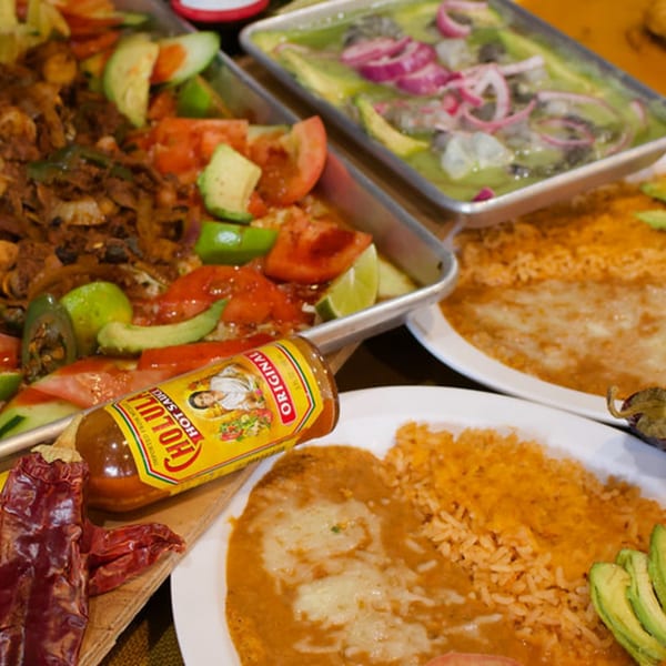 Mexican dishes including fajitas, ceviche, rice, beans, and a bottle of Cholula hot sauce.