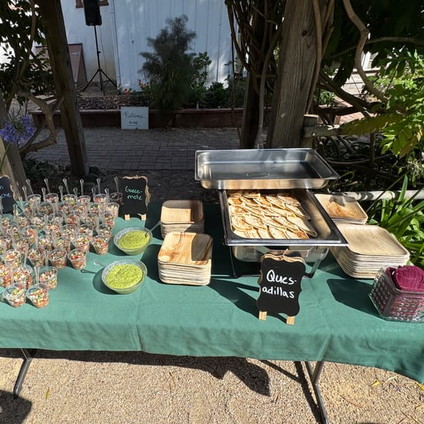 Outdoor La Parrilla Taqueria catering setup with quesadillas, guacamole, and ceviche cups on a green tablecloth.