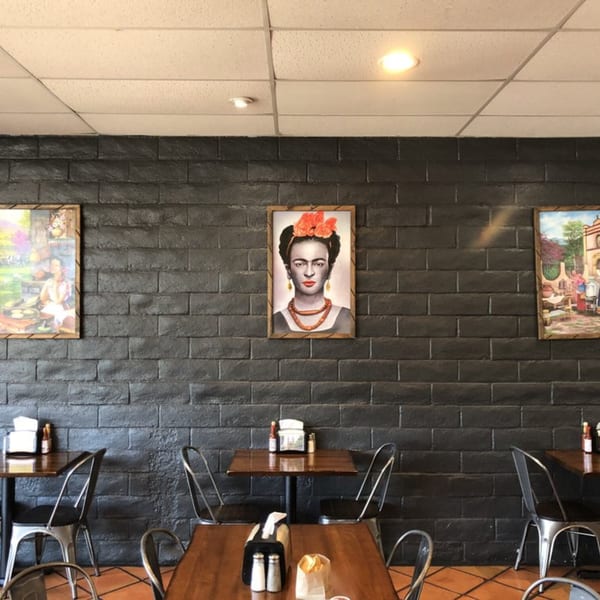 La Parrilla Taqueria's dining room with dark brick walls, Frida Kahlo art, and wooden tables with metal chairs.