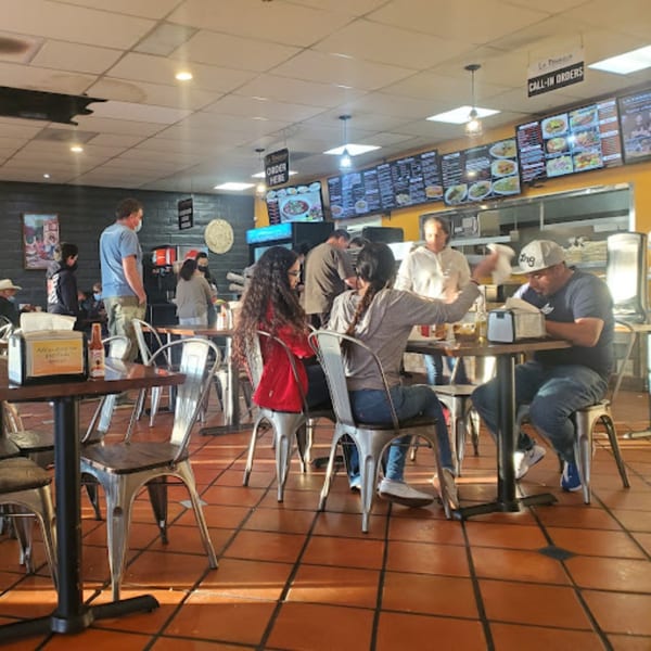 Diners seated at tables and standing near the counter in a casual Mexican restaurant.