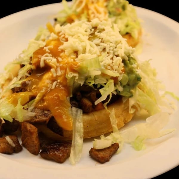 Two La Parrilla Taqueria sopes topped with meat, lettuce, cheese, guacamole, and orange sauce.