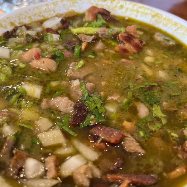 Close-up of a hearty Mexican soup with meat, beans, onions, and cilantro in a white bowl.