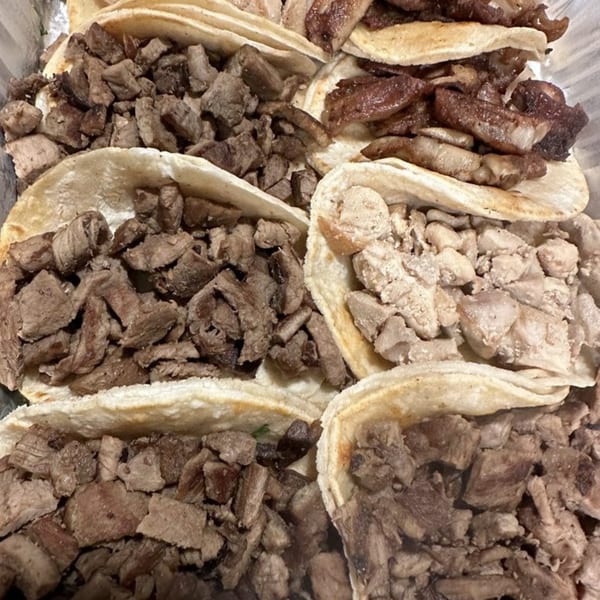 A close-up of several La Parrilla Taqueria tacos filled with various meats like steak and chicken.