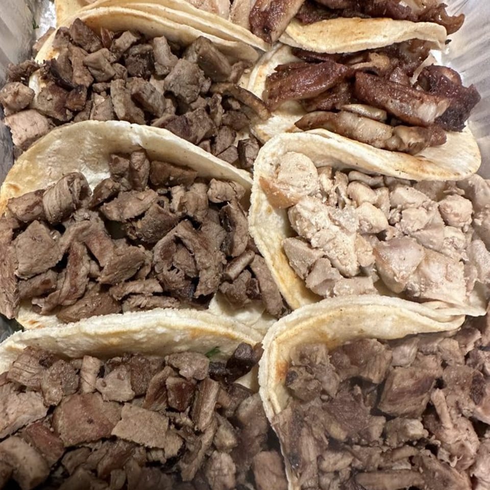A close-up of several La Parrilla Taqueria tacos filled with various meats like steak and chicken.